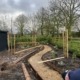 An image of a man bending down making a stone pathway laid through a soil area with new young trees and plants